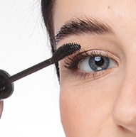 En kvinde påfører mascara med en børste og tilføjer volumen til sine vipper og perfektionerer sin øjenmakeup.