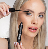 En kvinde påfører omhyggeligt mascara på sine øjenvipper og holder børsten tæt på for at få en perfekt finish.