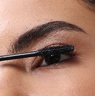 Et nærbillede af en person, der påfører Nanolash sort mascara på deres øvre øjenvipper med en wand.