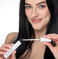 En kvinde holder elegant en tube Nanolash mascara og udstråler skønhed og selvtillid i en stilfuld setting.