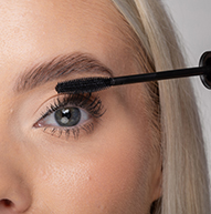 En kvinde bruger en mascarabørste til at påføre mascara og forbedrer dygtigt sine øjenvipper for et mere dramatisk udseende.