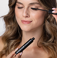 En kvinde påfører omhyggeligt mascara for at fremhæve sine øjenvipper og fokuserer intenst på sin makeup-rutine.