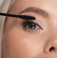 En kvinde påfører omhyggeligt mascara på sine øjenvipper med en mascarabørste og forbedrer sin øjenmakeup med præcision.
