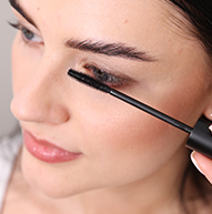 En kvinde bruger dygtigt en mascarabørste til at påføre mascara og fokuserer på sine øjenvipper for at opnå et defineret look.