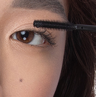 En kvinde påfører mascara med en børste og fokuserer på sine øjenvipper for at opnå et defineret og elegant look.